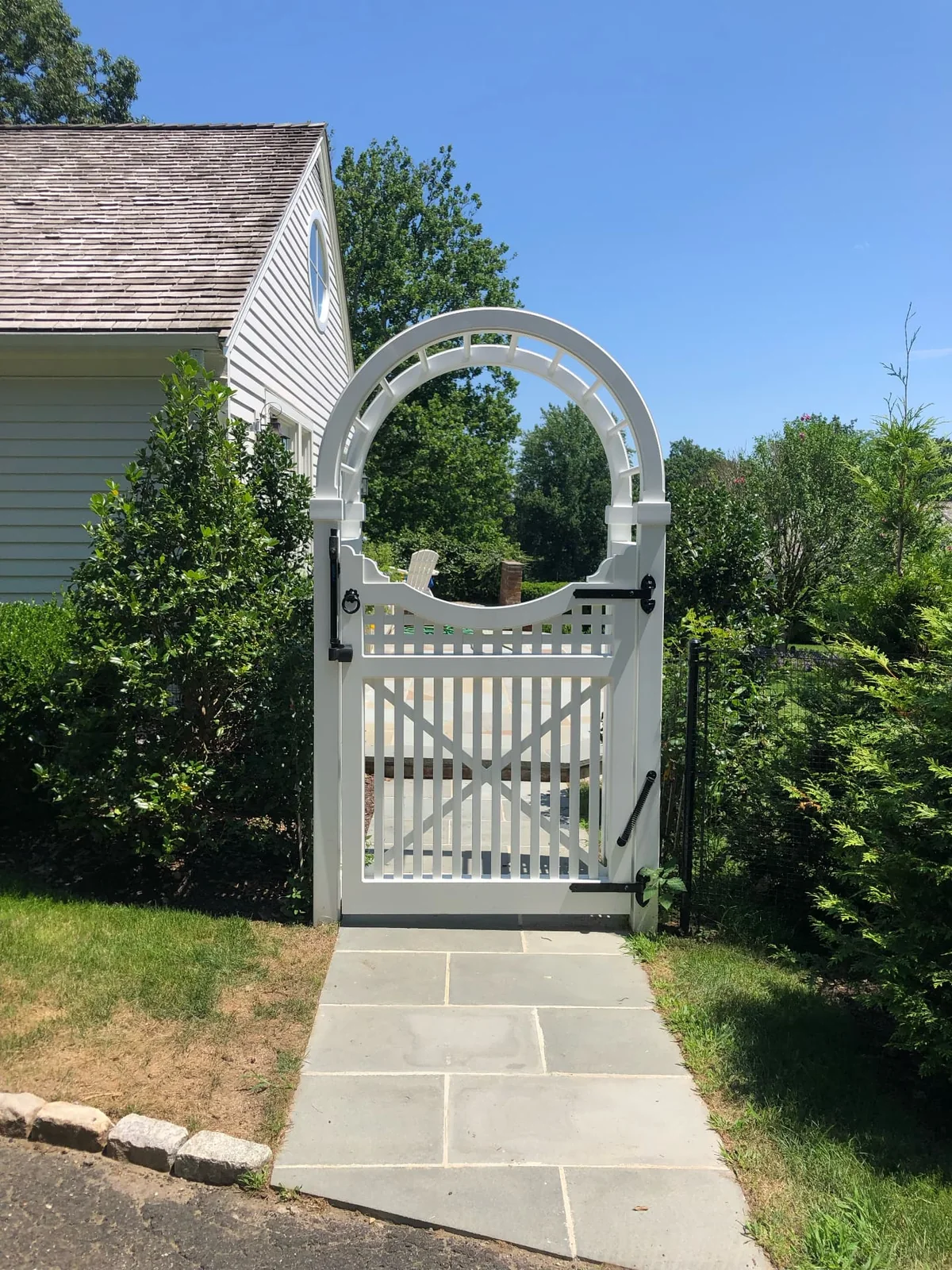 Custom white garden gate beneath a curved arbor