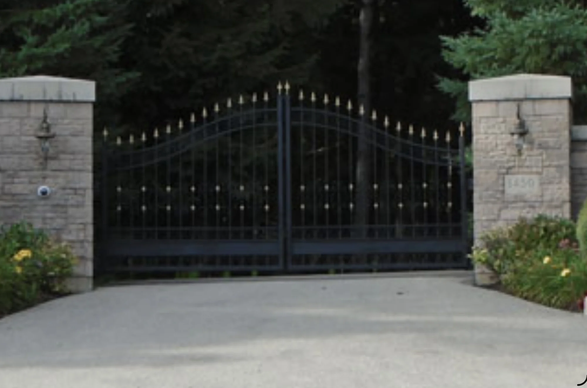 Curved black automated estate gate between stone pillars