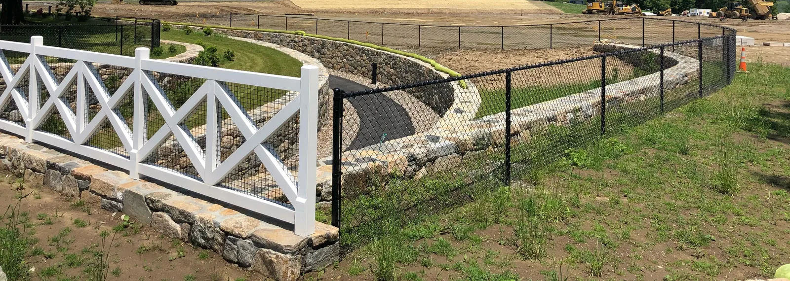 Custom white crossbuck fence and black chain link fence at a landscaped property