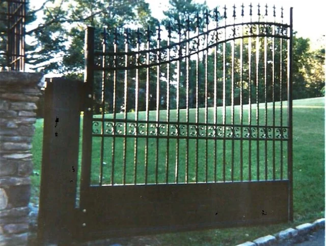 Arched black iron driveway gate with decorative pickets
